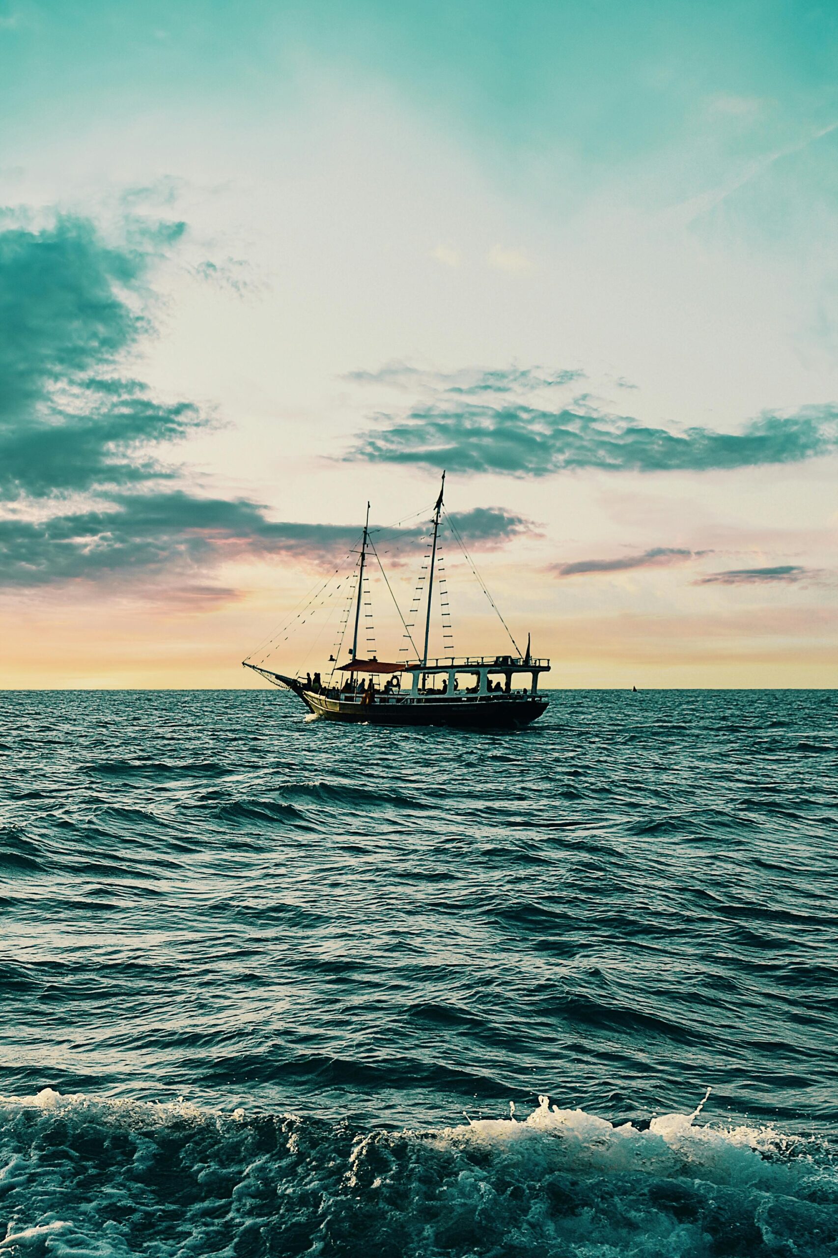A majestic sailing ship navigates open waters at sunset, against a vibrant sky.